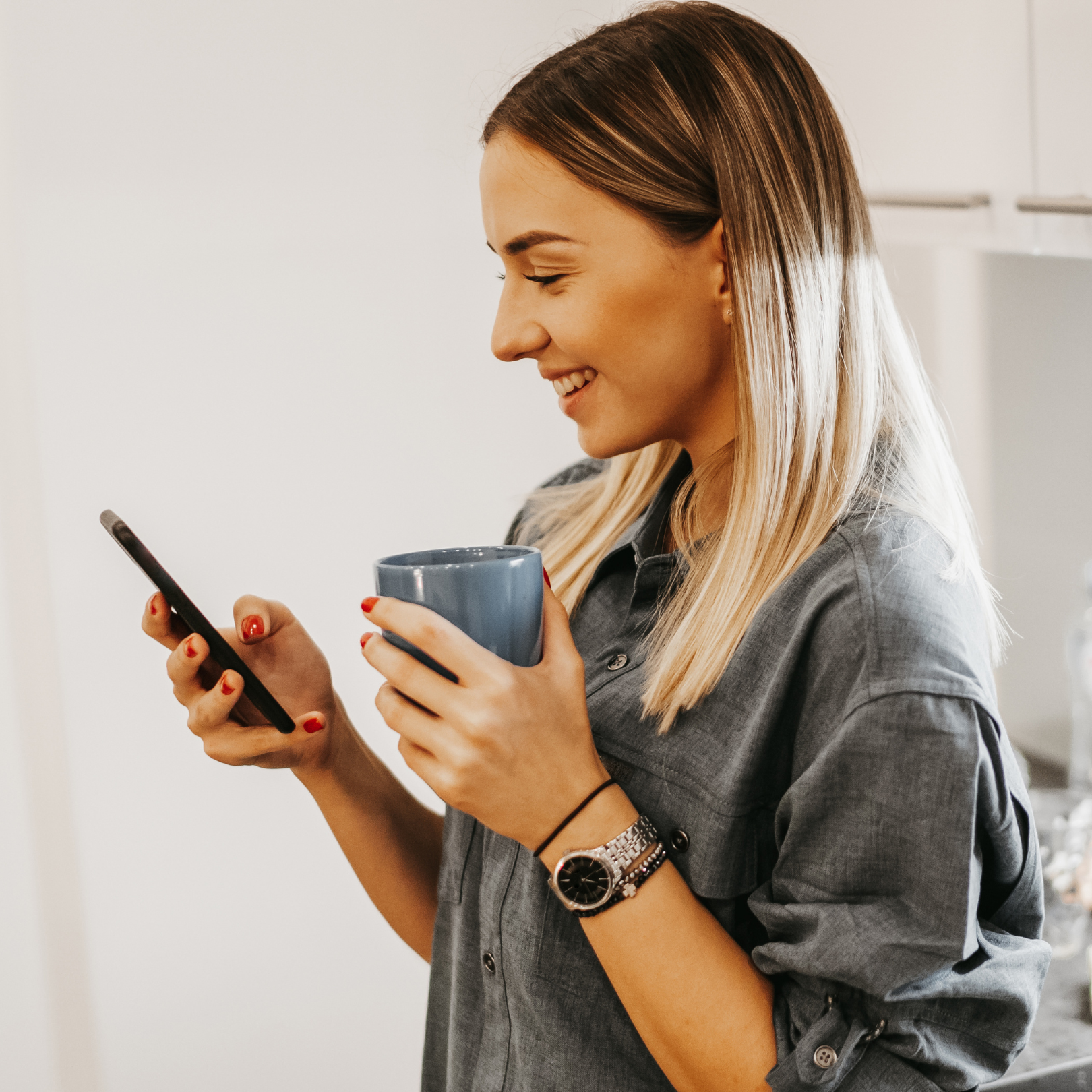 A girl smiling at her phone whilst holding a cup of coffee